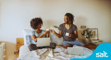 Two people at home on their beds busy with a morning routine of coffee and starting work from home.