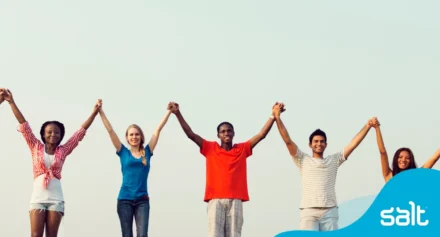 Diverse group of people standing side by side holding hands up in the air, representing allyship.