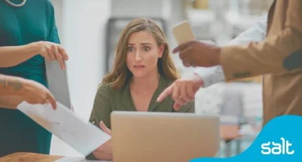 Woman looking anxious sat at her desk with too many people trying to speak to her at once.
