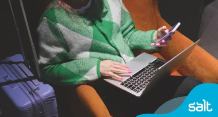 A freelancer working on laptop and phone with travel bag nearby.