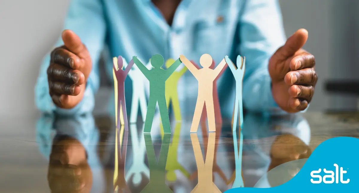 A man balancing between his hands a group of person shaped paper cut outs linked by hands