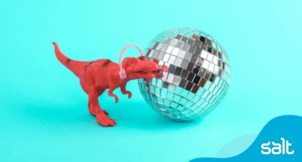 Playful red toy dinosaur with headphones and a disco ball, symbolising creativity, inclusion, and attracting autistic talent