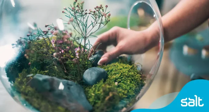 Close-up of a hand arranging plants and stones in a glass terrarium, symbolising growth and the benefits of external recruitment