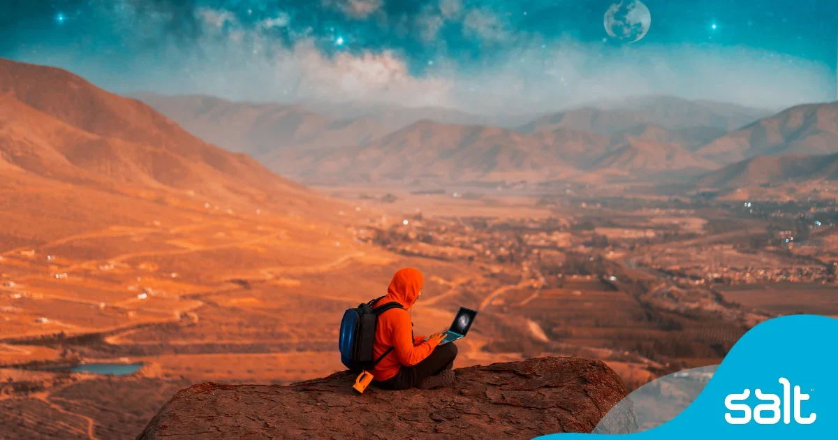 Man in red hoody sitting on-top of a mountain working on his laptop, symbolising a digital nomad