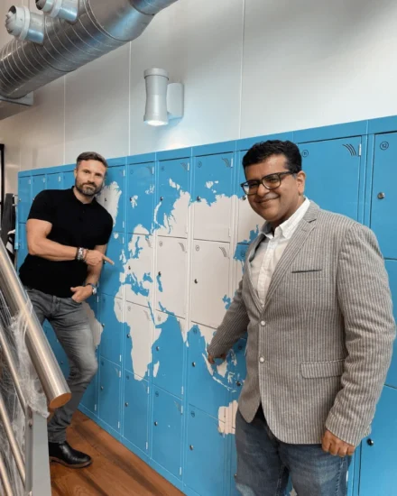 Two men smiling and pointing at different locations on company branded world map painted on blue lockers