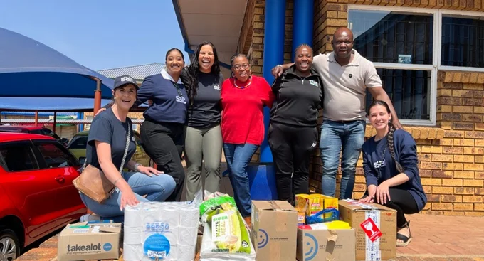 A cheerful group poses with donated goods outside a community building, highlighting a team effort in giving back and supporting local needs