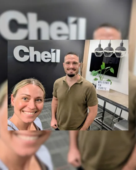 Two people smiling inside the Cheil office, with a welcome sign and company logo in the background
