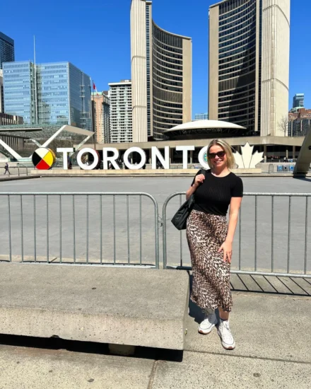 Woman posing in front of the TORONTO sign at Nathan Phillips Square on a sunny day