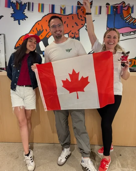 Three people celebrating and smiling with a Canadian flag indoors