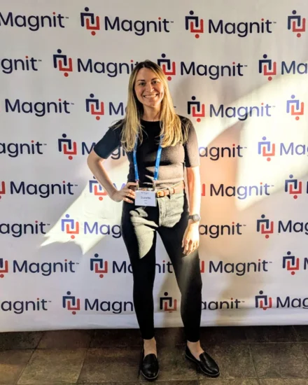 Woman smiling in front of a Magnit event backdrop wearing a name badge and conference lanyard