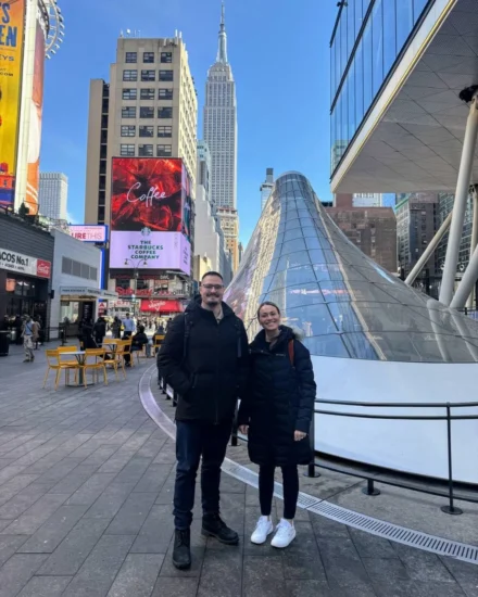 Two people bundled in winter coats posing in New York City with the Empire State Building in the background