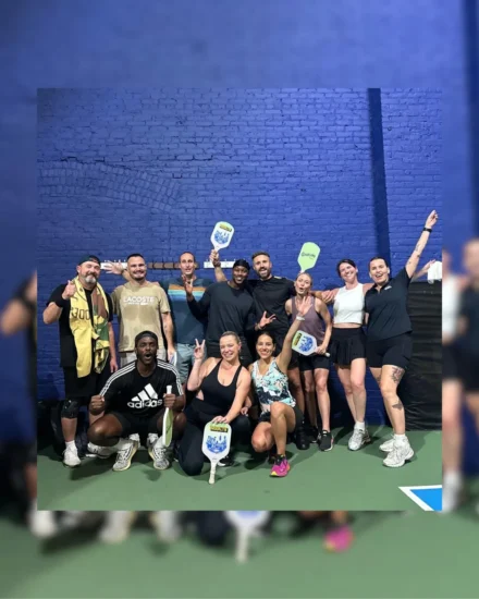 Group of people posing cheerfully with pickleball paddles on an indoor court