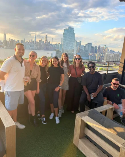Group of colleagues smiling on a rooftop with a stunning city skyline in the background during sunset