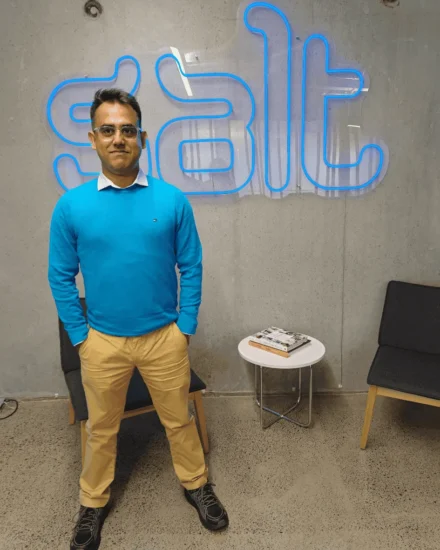 Man standing and posing in front of a neon "Salt" sign in an office space