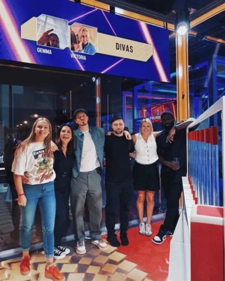 Group of six people posing and smiling in front of a vibrant game show-style set