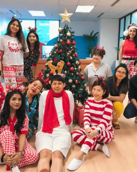 Group of people in festive outfits posing by a decorated Christmas tree in an office