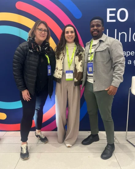 Three people wearing event badges smile for a photo in front of a colorful "AI Empowered" event backdrop.