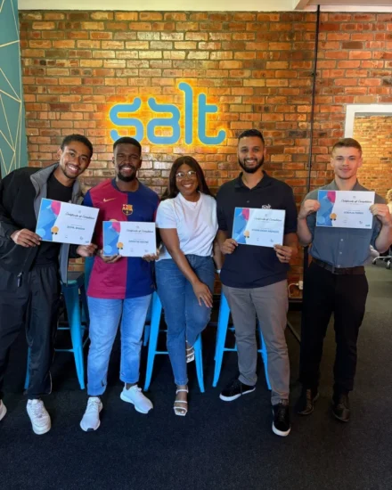 Five smiling team members pose in front of a Salt logo, four proudly holding certificates of completion after a training graduation.