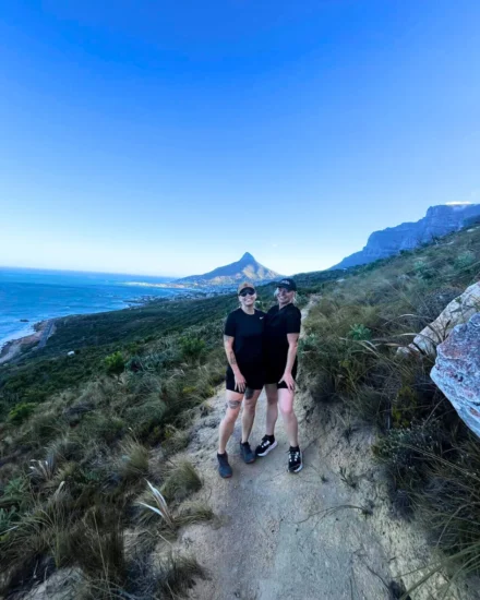 Two women smile on a hiking trail with ocean views and Lion’s Head mountain in the background in Cape Town.