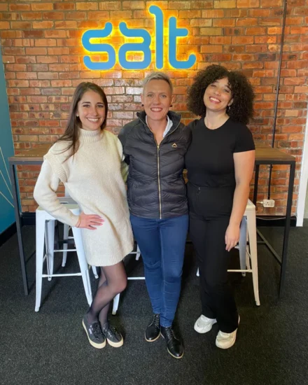 Three people smiling and posing in front of a Salt sign.