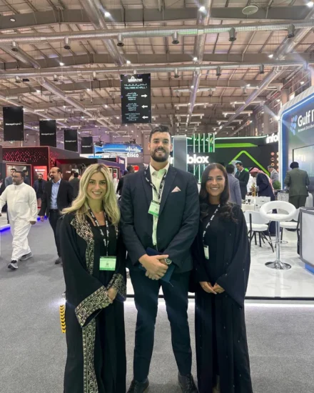 Three Salt team members posing at the Black Hat MEA cybersecurity event, surrounded by busy exhibition booths and attendees.