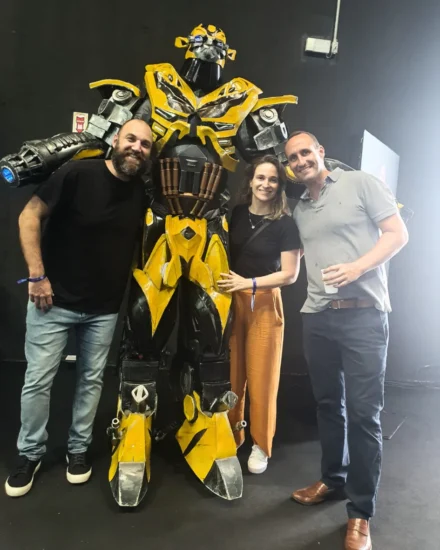 Three people smiling and posing with a person in a large yellow robot costume at the Rio Innovation week