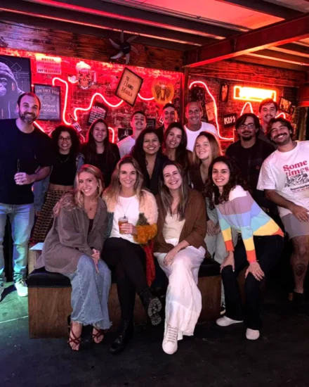 A group of colleagues smiling and posing together during a night out at a bar with neon lights and signs in the background