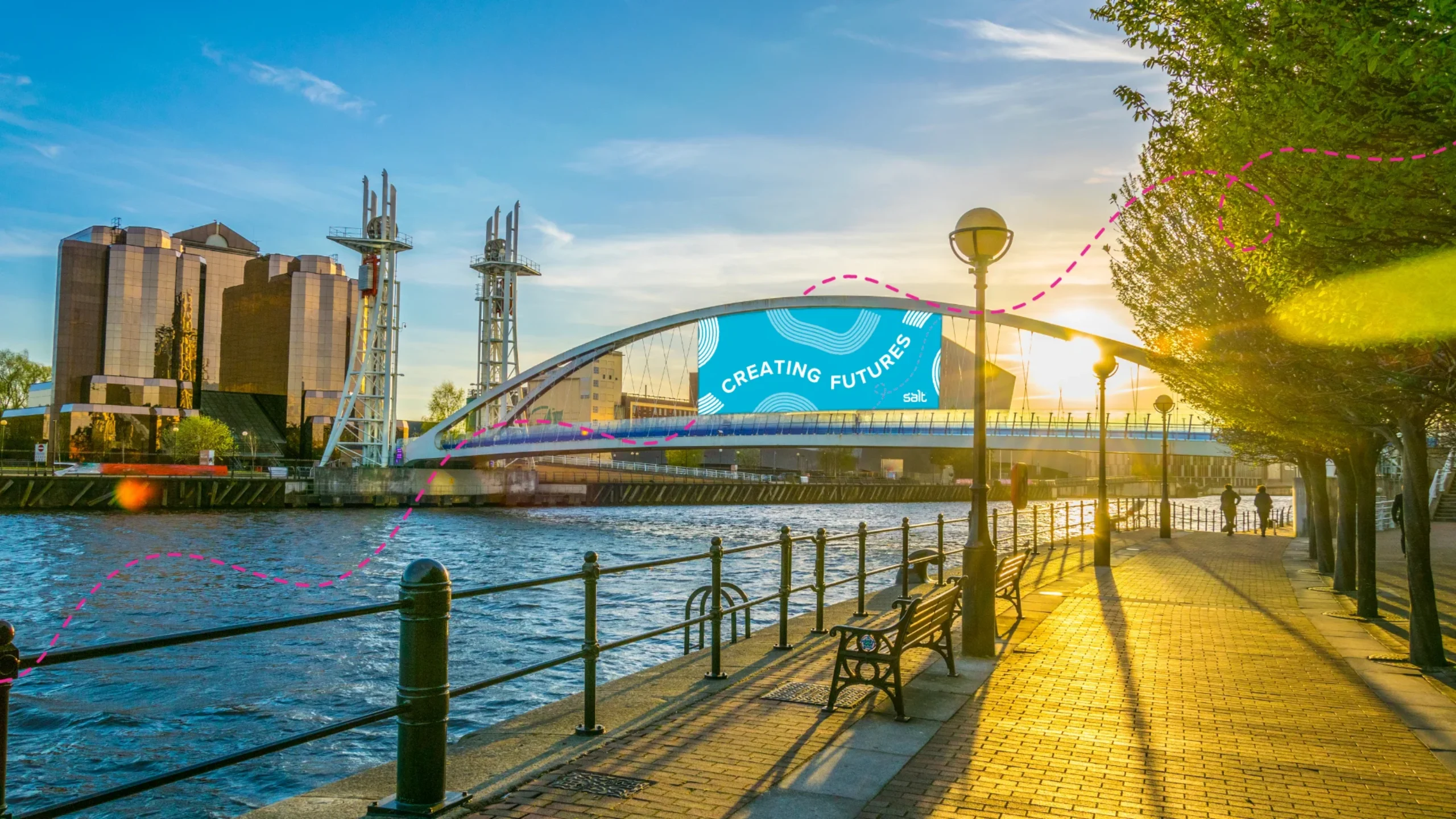 Sunset view of Salford Quays in Manchester, with a “Creating Futures” banner on the lift bridge over the canal