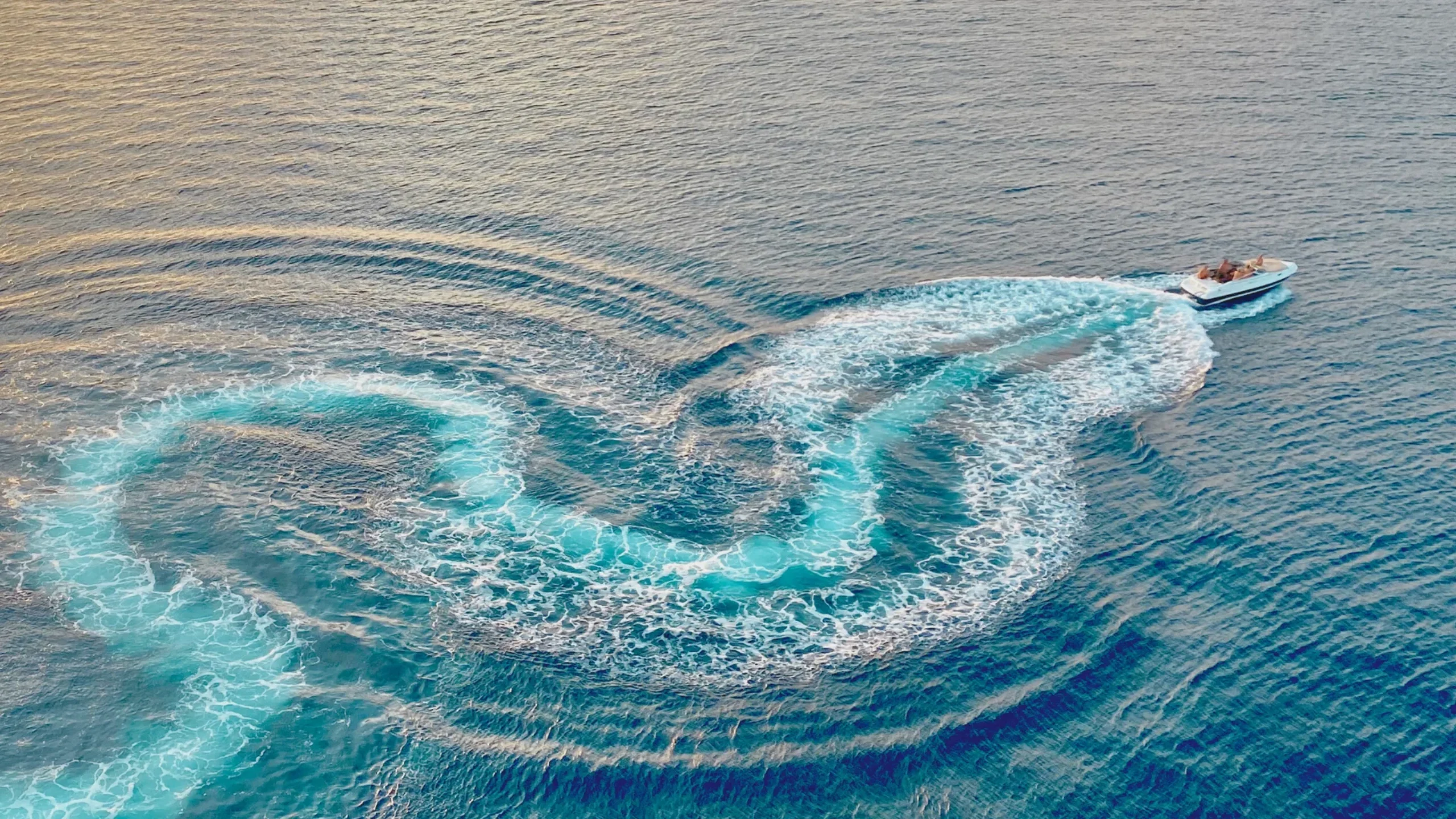 Boat making swirls behind it in the ocean in the golden hour