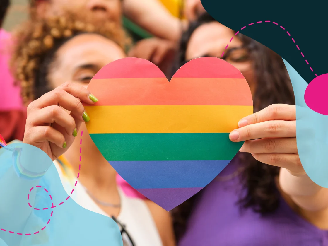 Two women holding a heart coloured in the pride rainbow.