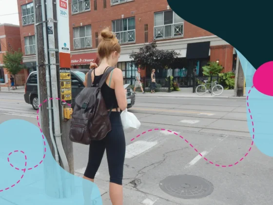 Woman waiting to cross a Toronto street, she is on her phone while she waits.