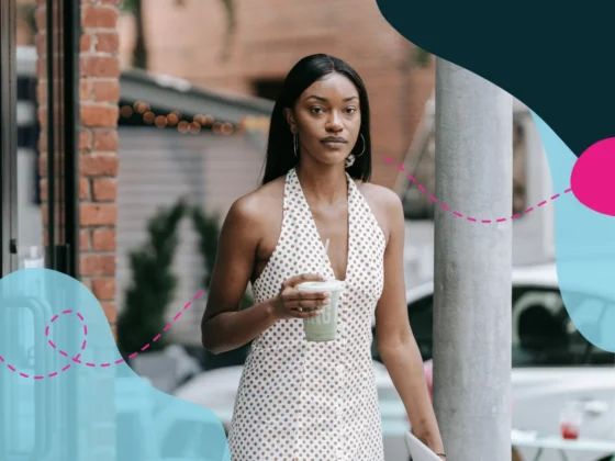 Woman walking out of a coffee shop on to the side walk with a takeaway coffee in her hand.