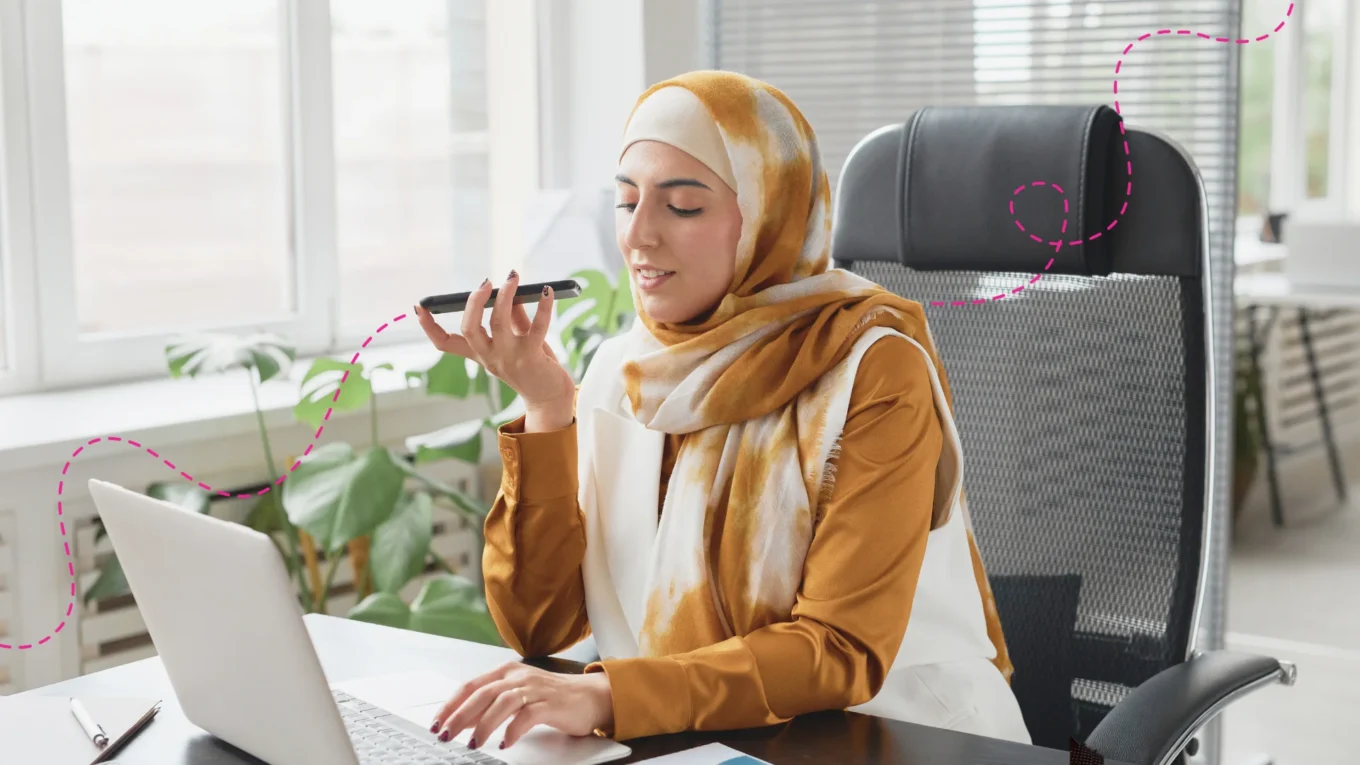 Emirate woman sitting at her desk on a call and working on her laptop.