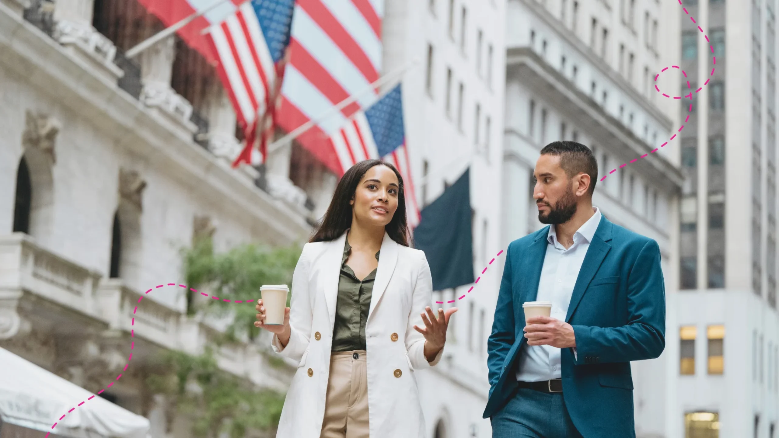 Two business colleagues walking on a sidewalk having a conversation — in the background there are American flags.