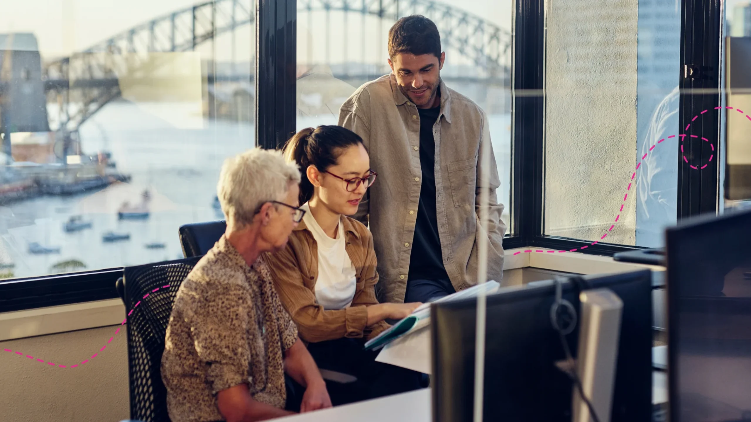 Three people looking at a computer together in an office with Sydney Harbour bridge in the background.