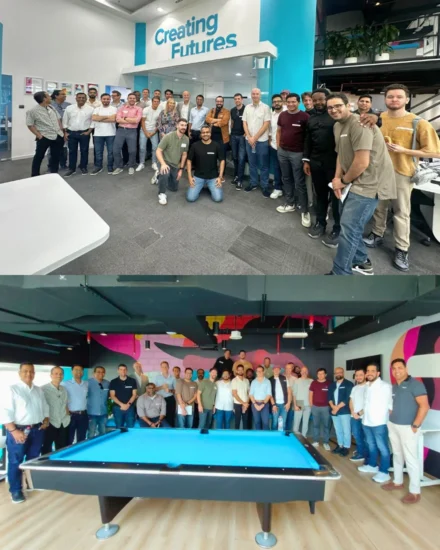 A large group of people posing together in an office environment and a recreational area with a pool table, smiling at an event.