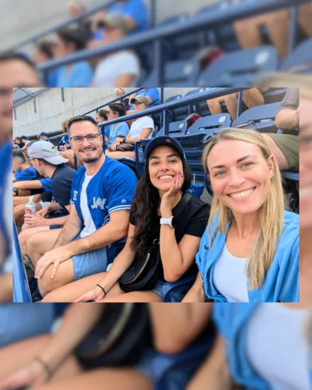 Three colleagues smiling in stadium seats at a baseball game, with fans in the background.