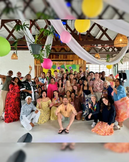 Large group smiling and posing at a colourful tropical-themed party indoors.