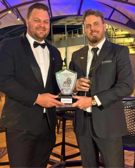 Two men, including the Africa Director and Founder, Alex Martin, in formal suits smiling and holding an award trophy at an evening event.